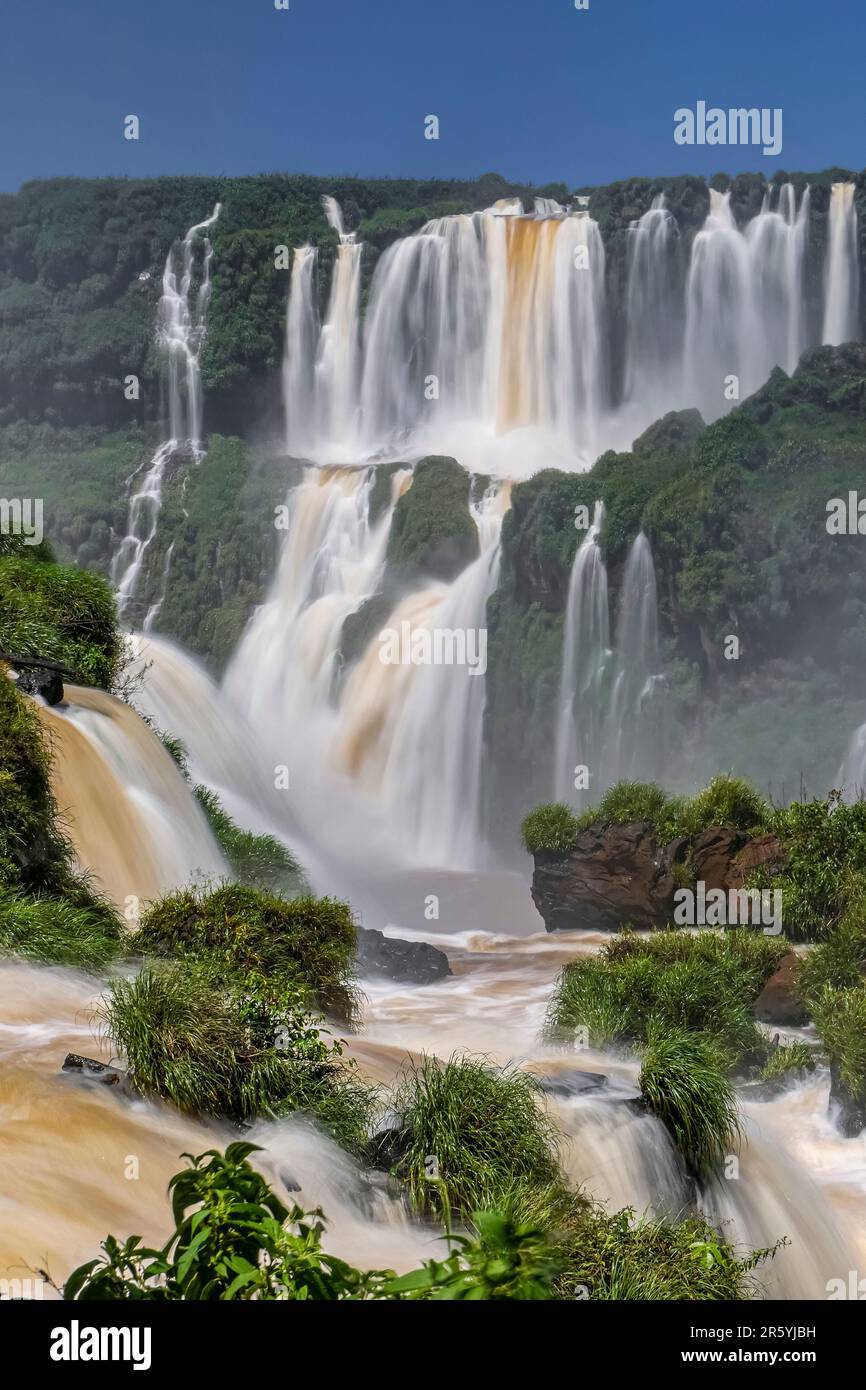 Spektakuläre Iguazu-Fälle mit blauem Himmel und üppiger grüner Vegetation Stockfoto