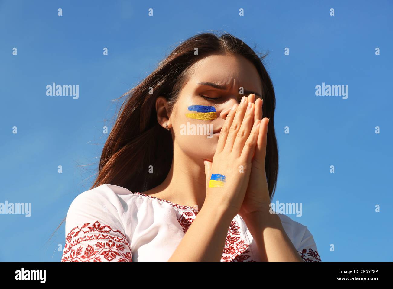 Junge ukrainische Frau mit gefalteten Händen am blauen Himmel Stockfoto