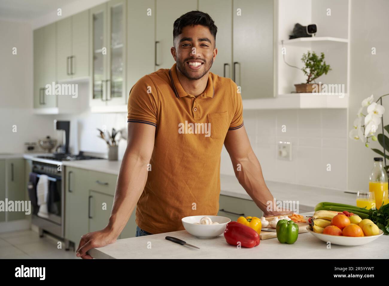 Glücklicher junger birassistischer Mann in lässiger Kleidung, der neben Essen in der Küche auf die Kamera schaut Stockfoto