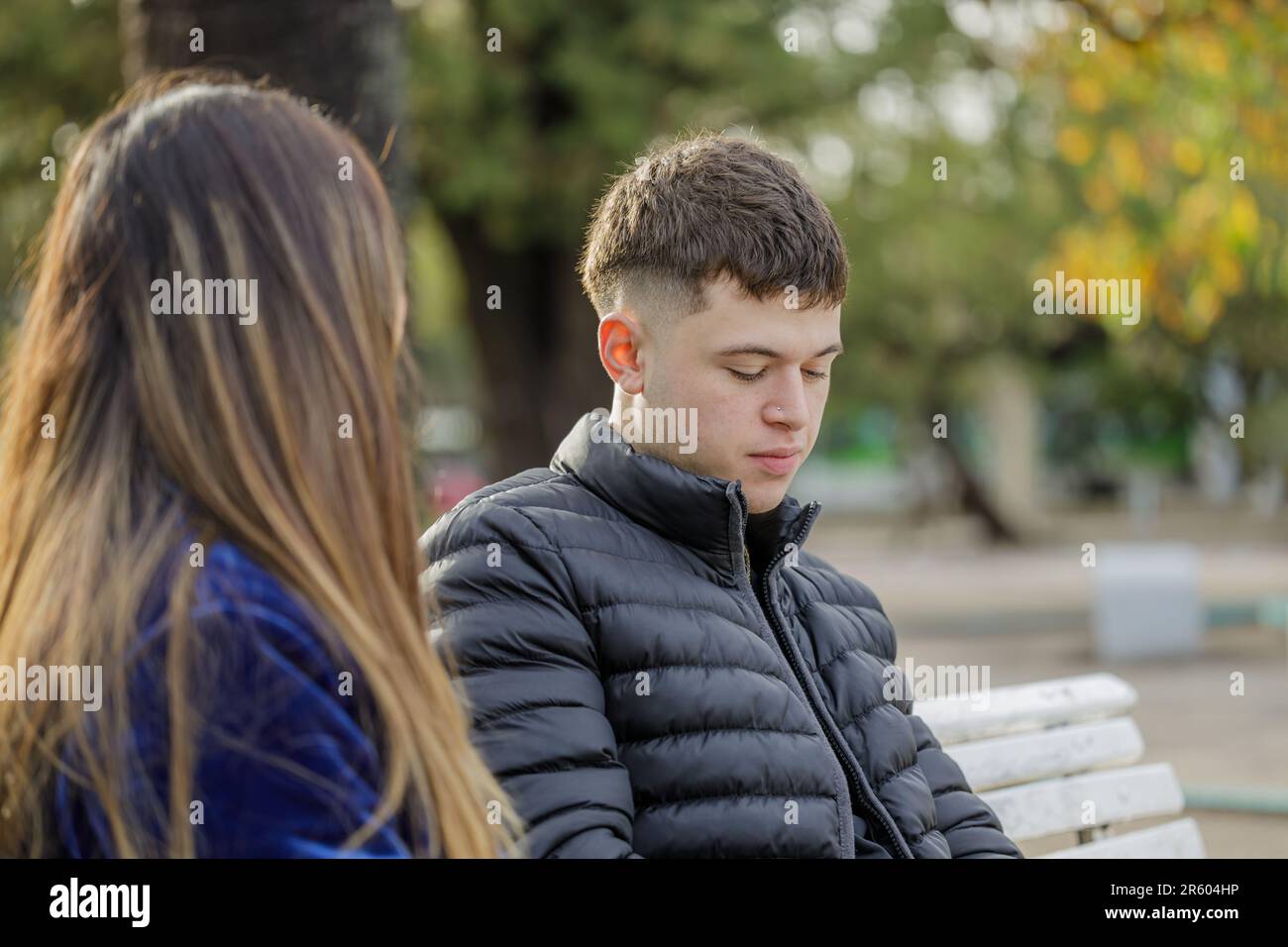 Ein Junge mit einer melancholischen Geste, der auf einer Bank neben einem Mädchen sitzt. Stockfoto