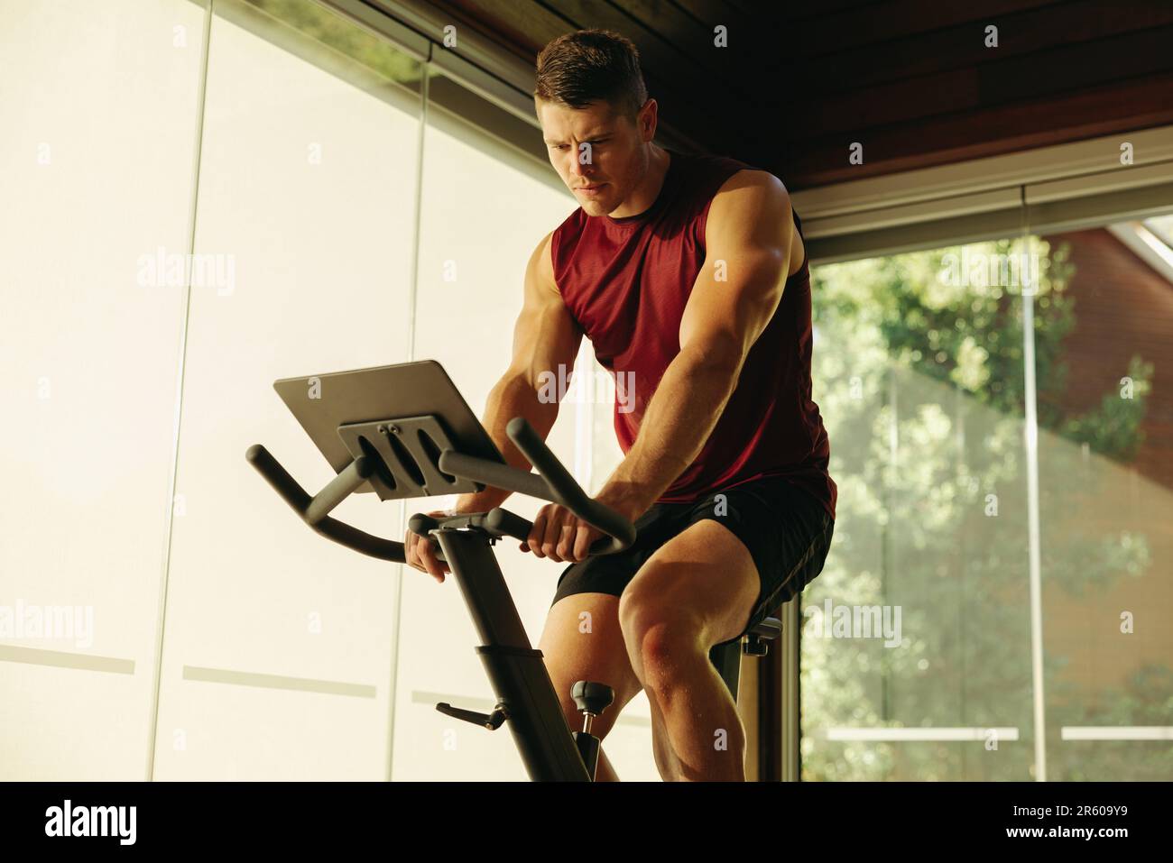 Ein Mann, der sich der Verbesserung seines allgemeinen Wohlbefindens verschrieben hat, indem er ein High-Tech-Fitness-Bike in seine Heimtrainingroutine integriert hat, indem er digitale Fitnessgeräte verwendet Stockfoto