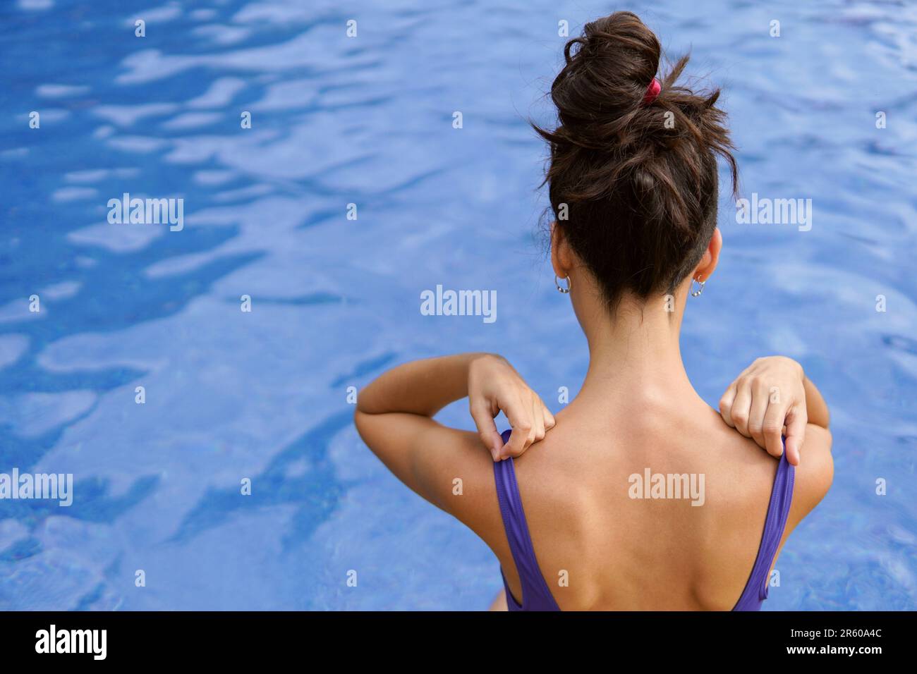 Eine magersüchtige schlanke Frau, die im Sommerurlaub in einem Swimmingpool sitzt Stockfoto