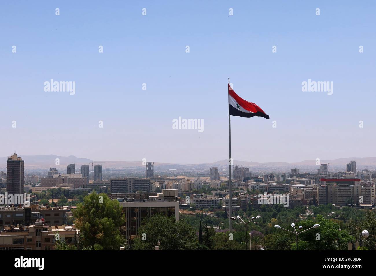 Damaskus, Syrien. 05. Juni 2023. Vor der Skyline von Damaskus steht eine syrische Flagge, die vom Berg Qasioun, Syrien, vom Juni 5 2023 aus gesehen wird. (Foto: Elisa Gestri/Sipa USA) Kredit: SIPA USA/Alamy Live News Stockfoto