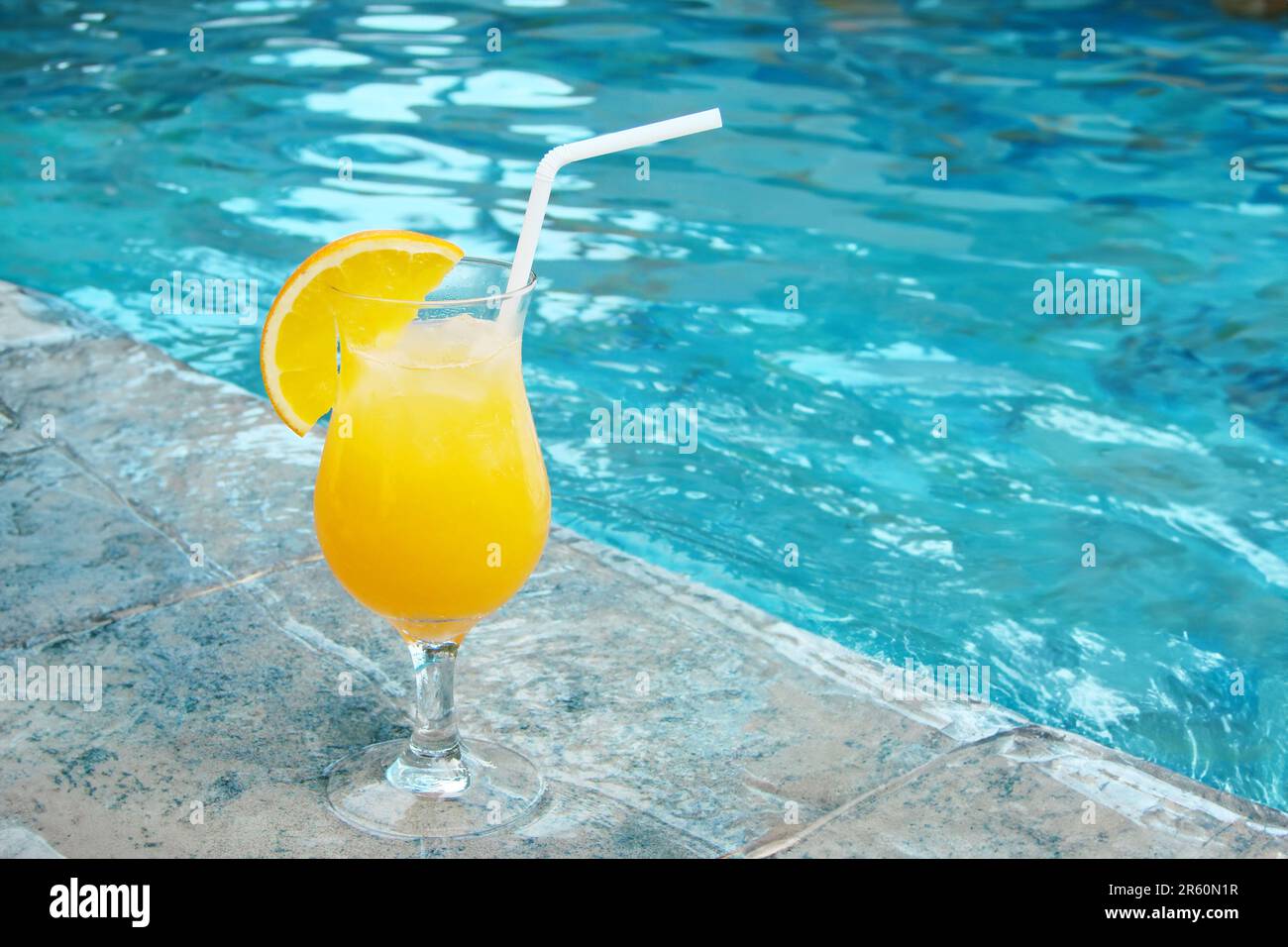 Ein Glas Orangensaft mit einem Strohhalm am Swimmingpool Stockfoto