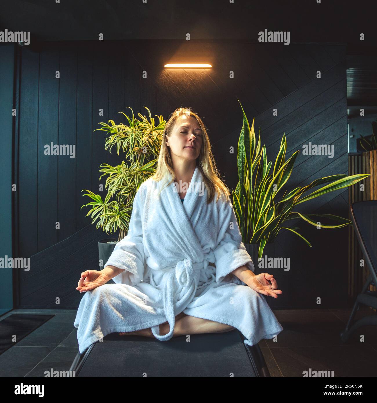 Frau im weißen Bademantel meditiert auf dem Sofa und entspannt sich zu Hause. Stockfoto
