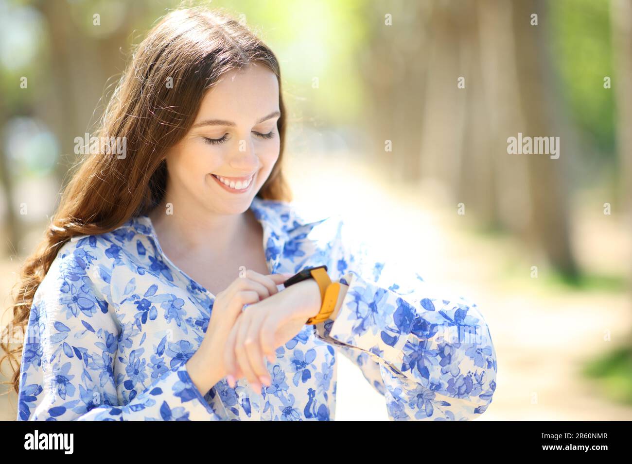 Glückliche Frau, die im Park auf Smartwatch schaut Stockfoto