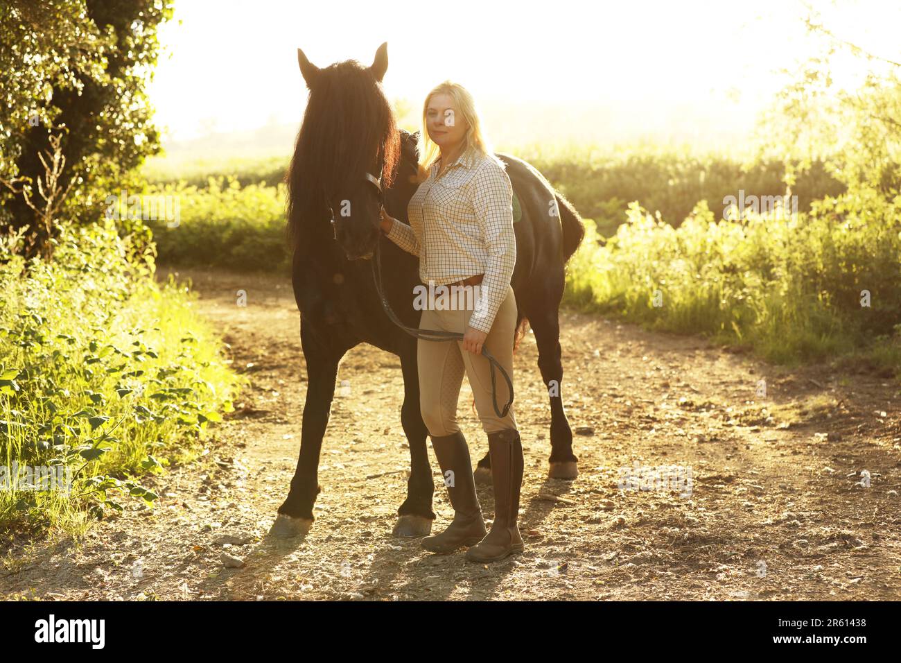 Eine blonde Frau, die mit einem schwarzen Pferd an einem sonnigen Abend steht Stockfoto