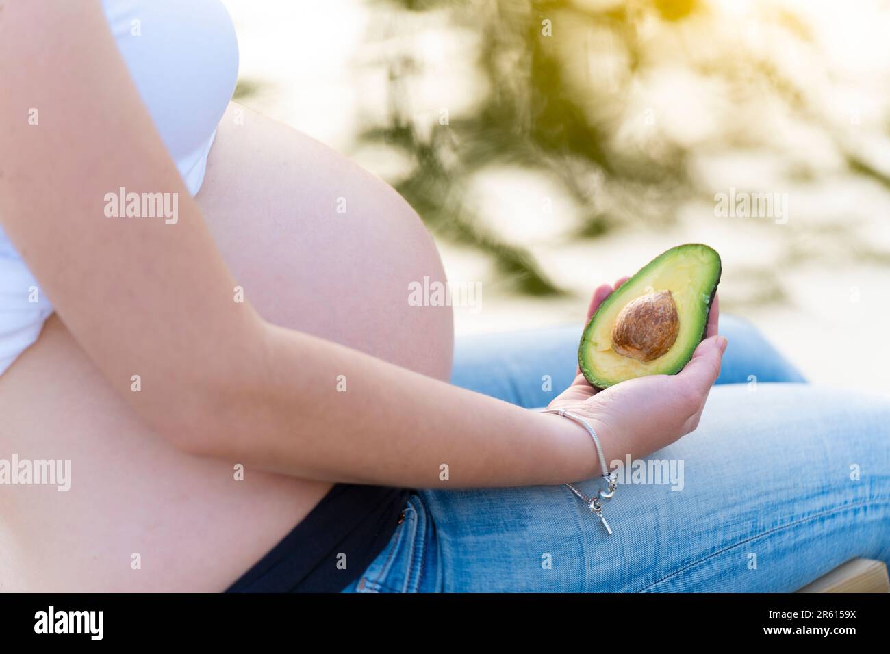 Schwangere Frau hält eine Avocado und zeigt sie der Kamera Stockfoto