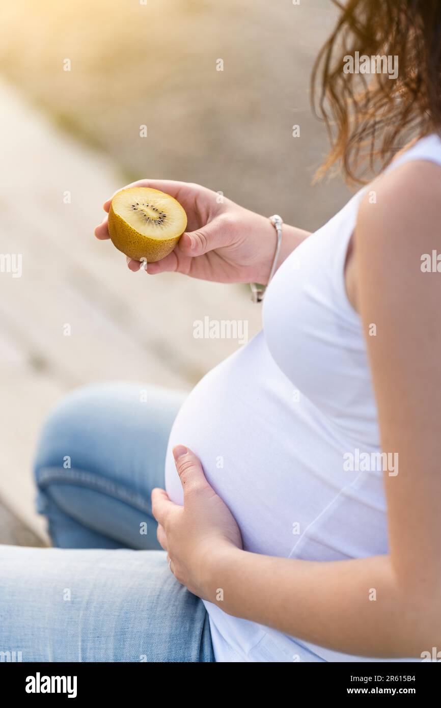 Schwangere Frau hält eine goldene Kiwi im Park Stockfoto