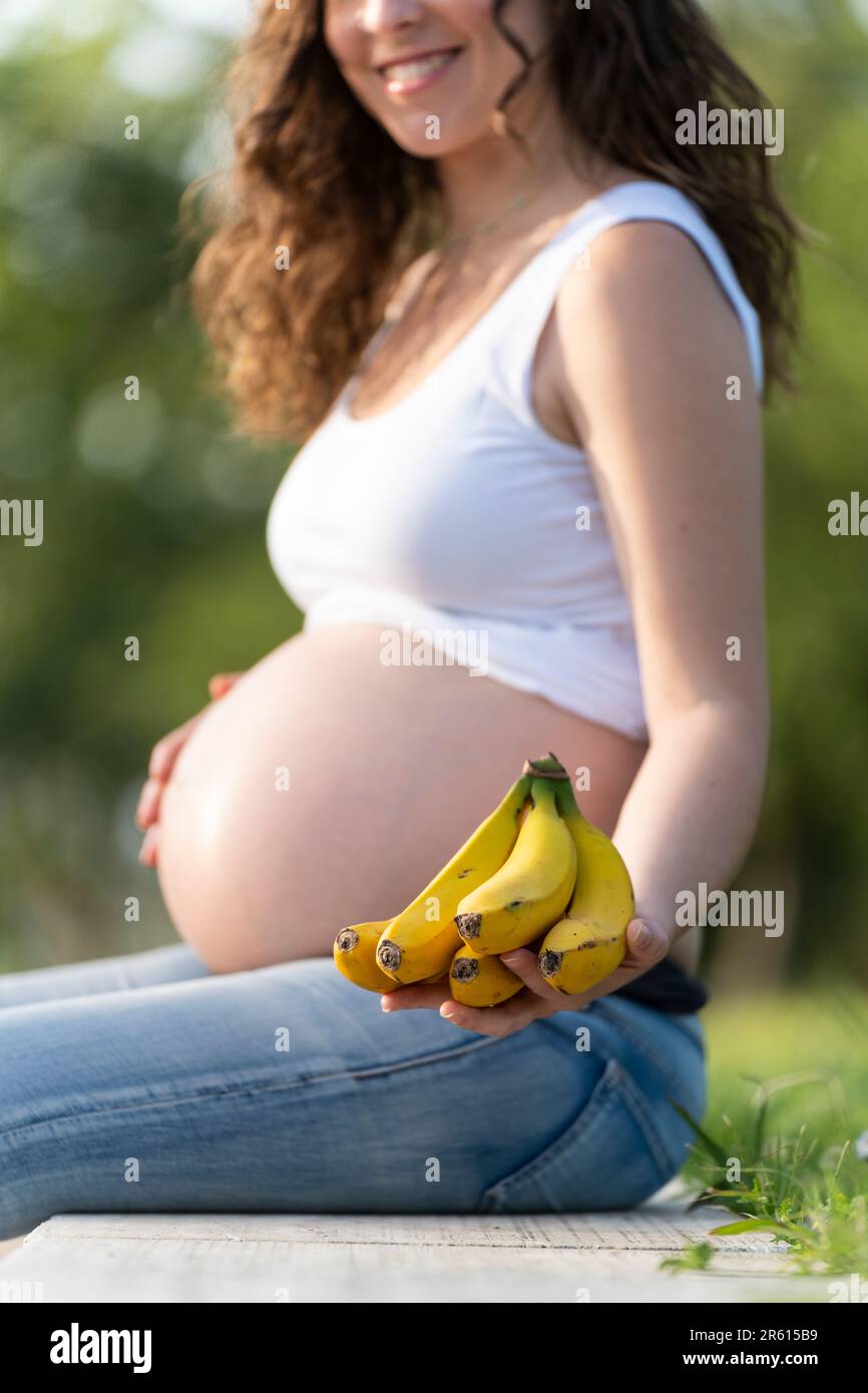 Schwangere Frau, die Bananen in der Hand hält und in die Kamera zeigt Stockfoto