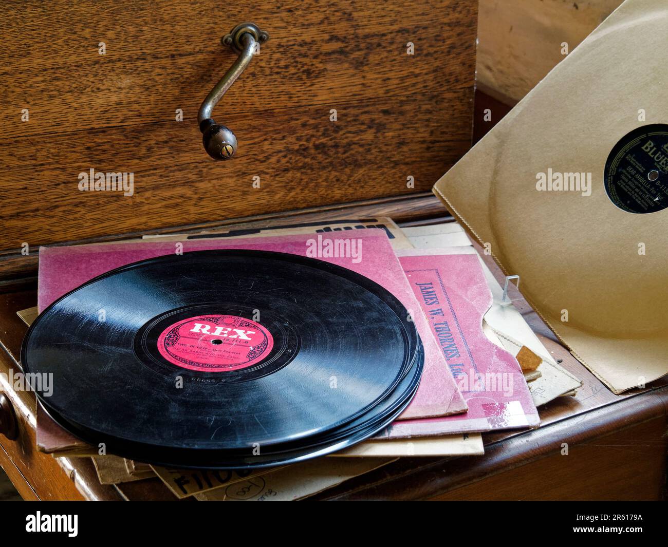 Alte 78-U/min-Schallplatten (78s), einige in ihren Ärmeln, zusammen mit einem aufziehbaren Grammophon aus Holz, wie es in der ersten Hälfte des 20. Jahrhunderts verwendet wurde. Stockfoto
