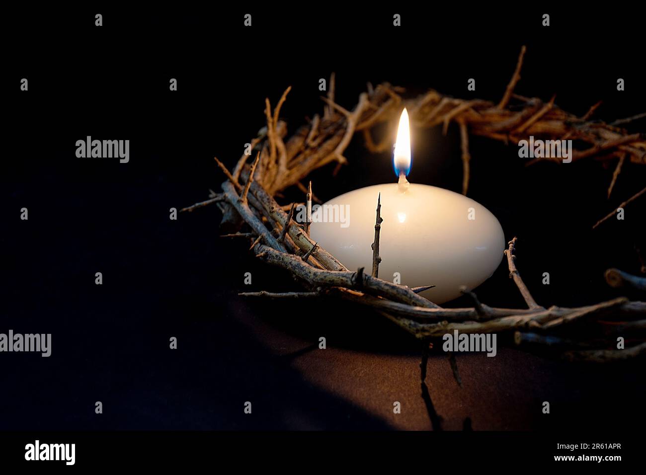 Nahaufnahme einer Dornenkrone mit einer glühenden Kerze auf Schwarz Stockfoto