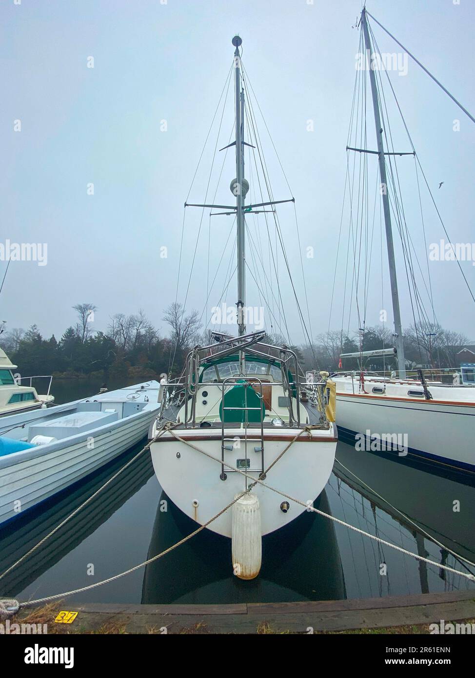 Vertikaler Blick auf die Rückseite eines Segelboots, das an einem nebligen Wintermorgen in einem Yachthafen festgebunden ist. Stockfoto