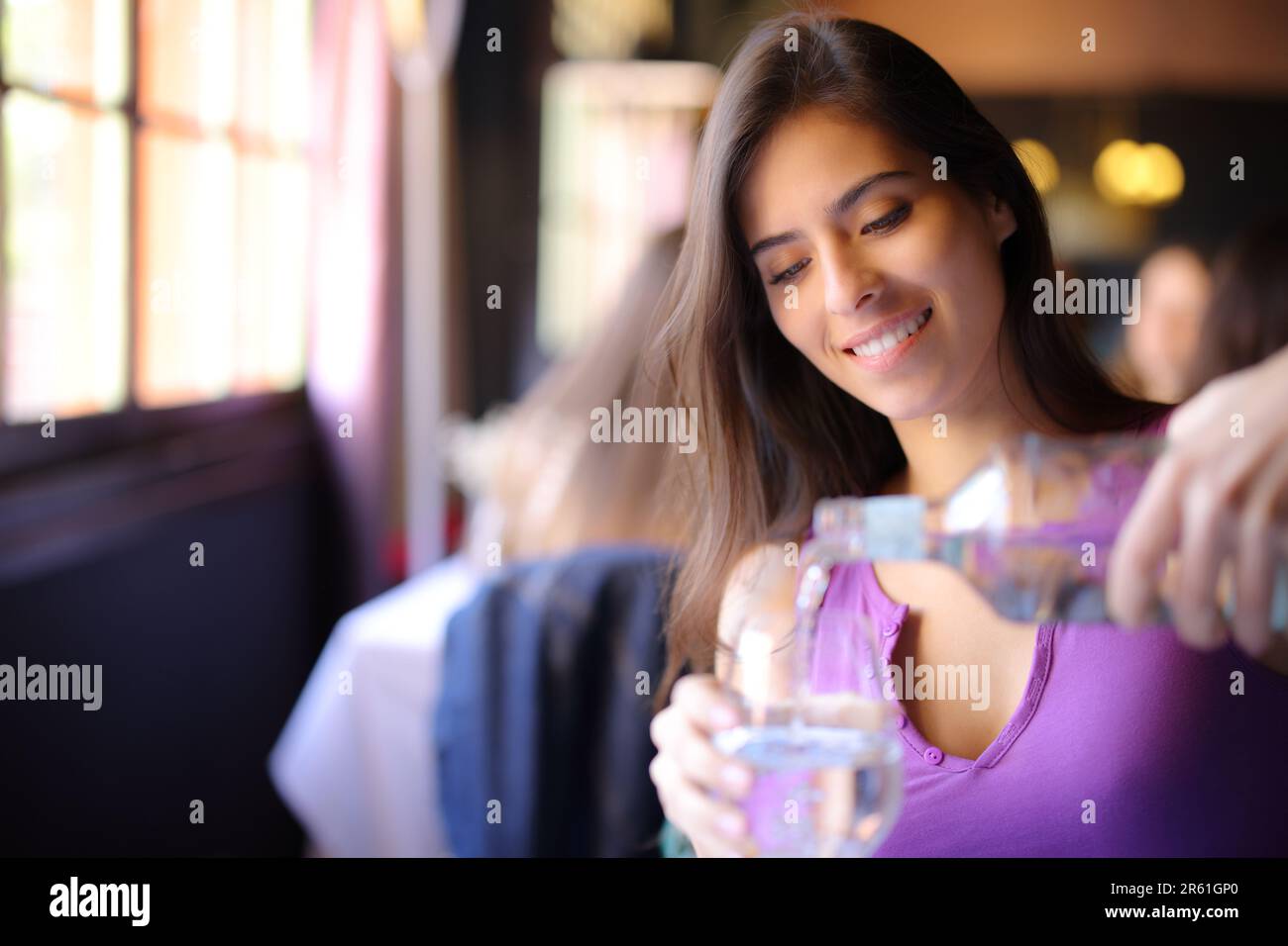 Glückliche Frau, die ein Glas mit Wasser in einem Restaurant füllte Stockfoto