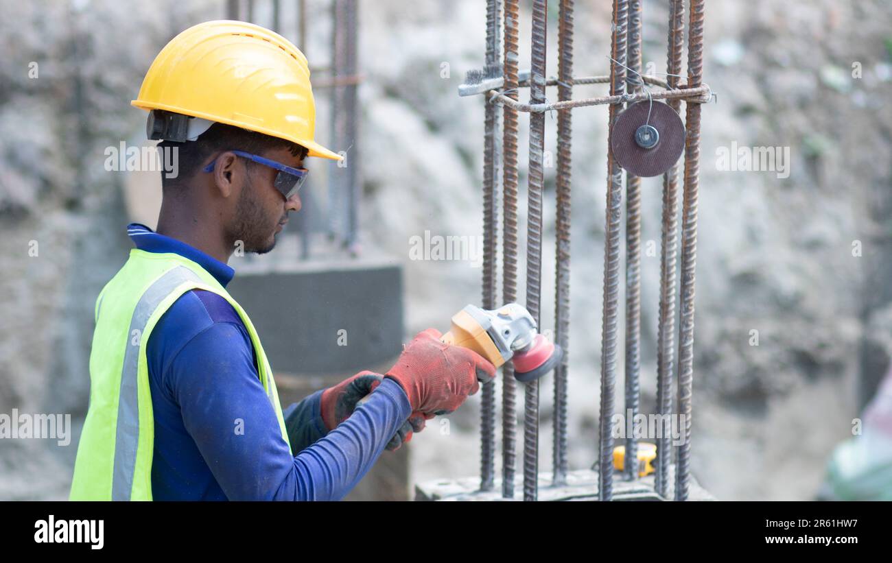 Bei Baukonzepten zeigt ein Bauarbeiter, der auf der Baustelle mit einem gelben Schutzhelm arbeitet, auf einen Winkelschleifer in seiner Hand. Professionell Stockfoto
