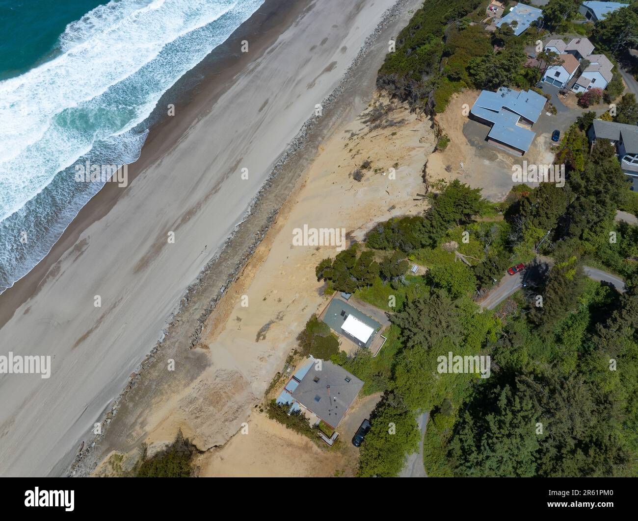 Nach der Zerstörung von Strandhäusern in Glen Eden Beach, Oregon, besteht nur noch eine Sandrutsche, die von der Zerstörung durch die Küstenerosion bedroht ist. Riprap - ein Gebilde aus großen Felsen - schützt vor steigendem Meeresspiegel an der Küste Oregons des Pazifischen Ozeans. Die befristete Maßnahme kann über $1000 € pro Fuß kosten und wird in diesem Fall vom Hauseigentümer getragen. Stockfoto