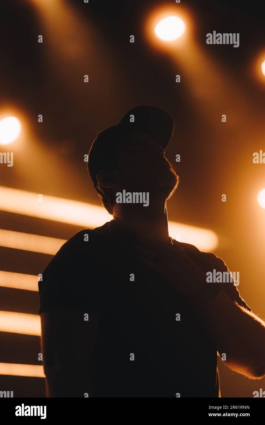 Die Silhouette eines Mannes mit Hut, der ein Konzert genießt, das von einer Lichtshow beleuchtet wird Stockfoto