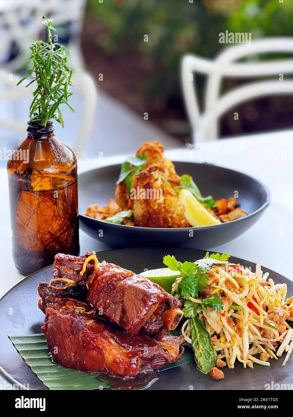 Eine saftige Platte mit gegrillten Schweinerippchen, begleitet von einem lebhaften grünen Papayasalat im thailändischen Stil, präsentiert auf einem weißen Teller Stockfoto