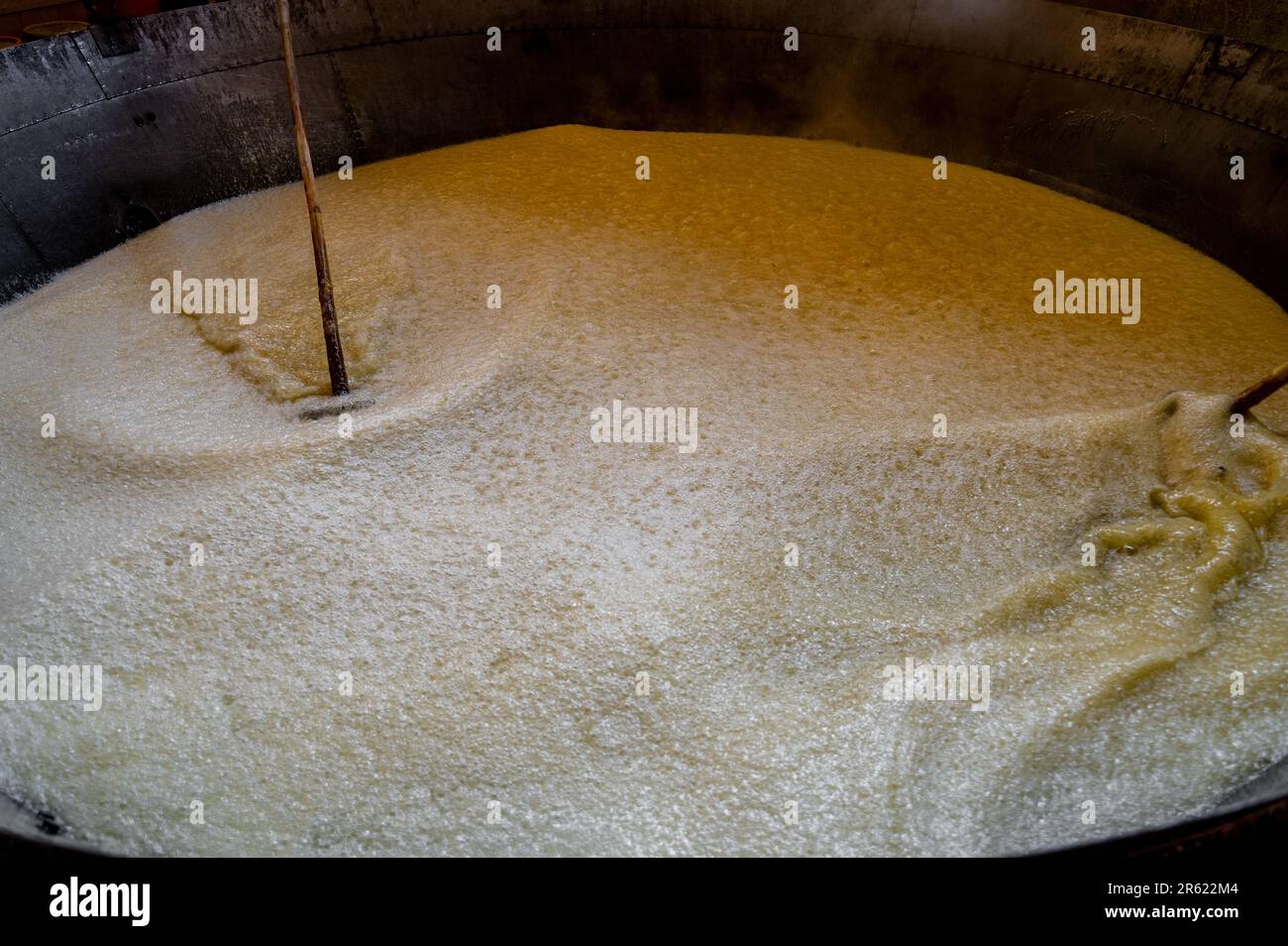 Während der Zuckerrohrherstellung rührt der Zuckerrohrsaft mit Hilfe von Holzbambusstäbchen zur Konzentration in einem großen Utensil. Während der Herstellung von Stockfoto