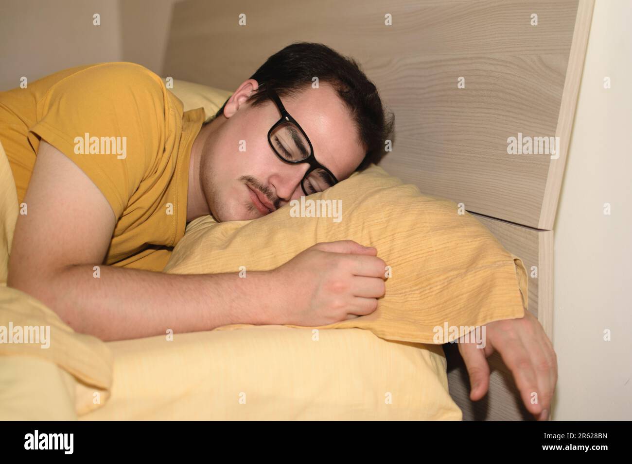 Ein junger Mann mit schwarzer Brille schläft im Bett. Stockfoto