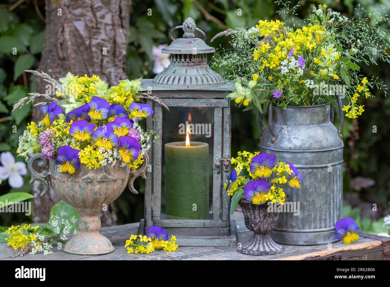 Blumenarrangements mit Blüten aus blauen Violaflumen, gelbem Bettstroh und Wiesenblumen in Vintage-Vasen Stockfoto