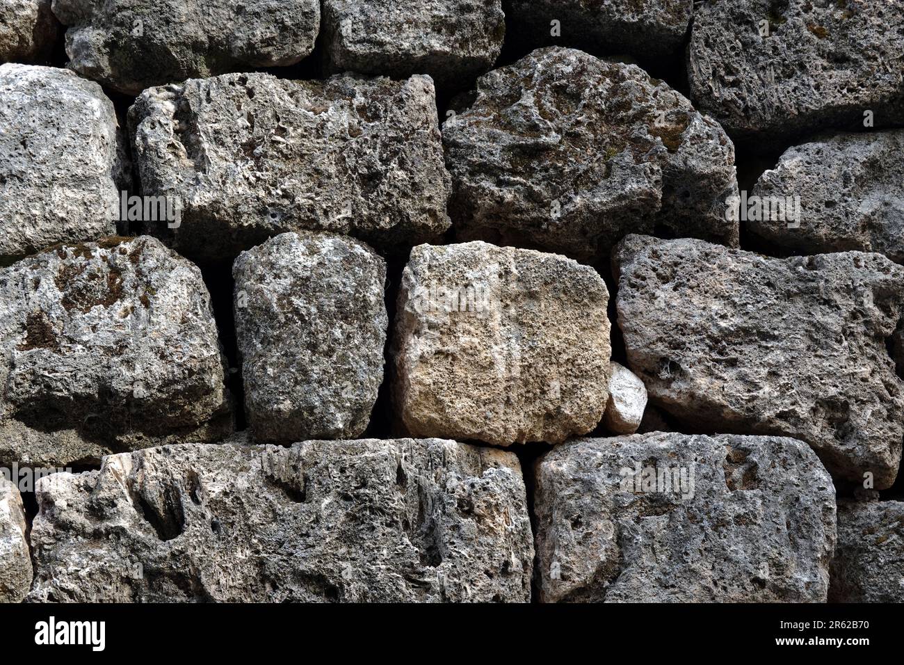 Alte Steinarbeiten aus alten, großen Natursteinen als Hintergrund mit Vegetation, die in Nahaufnahme durchbricht Stockfoto