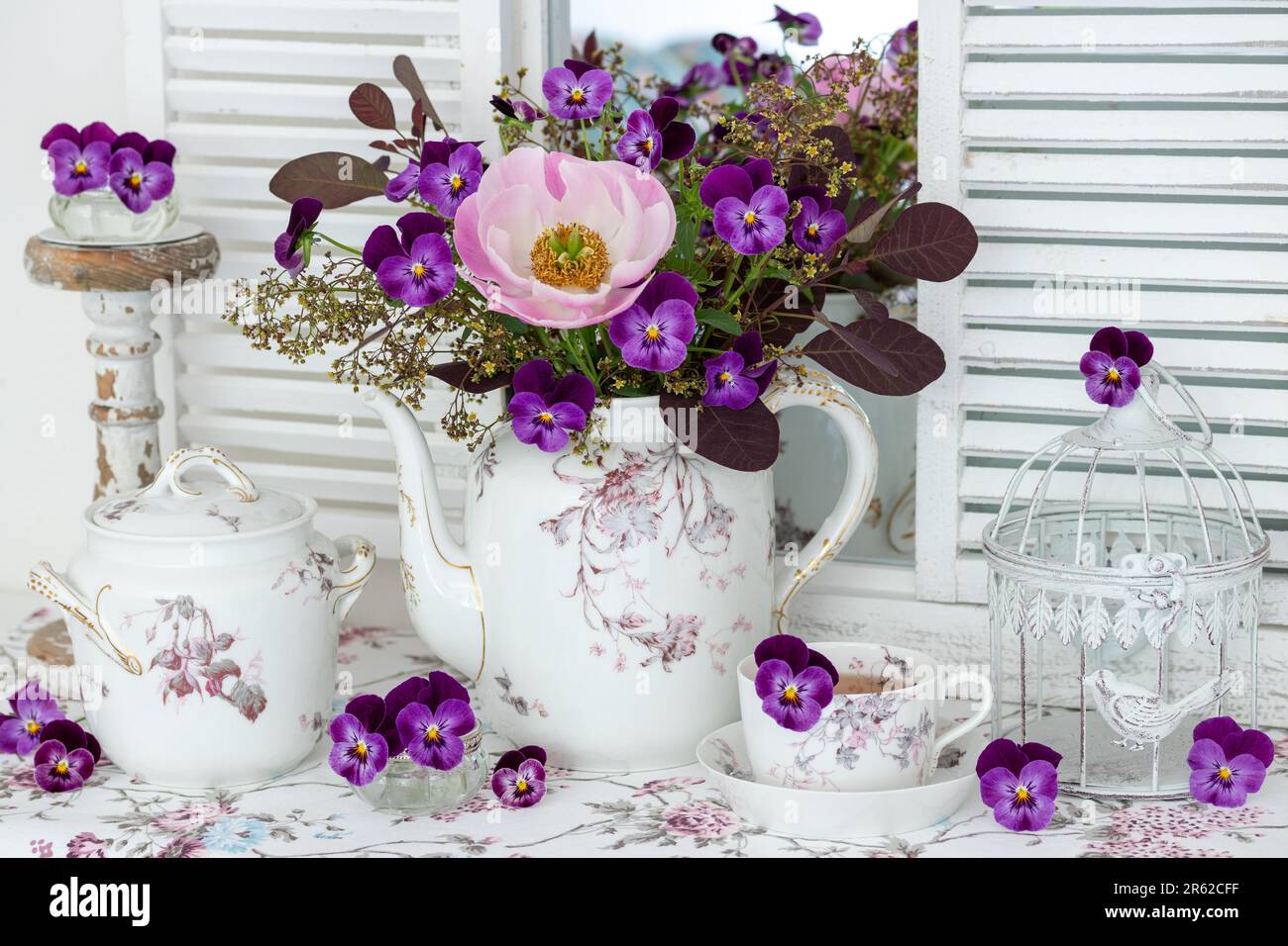 Arrangement mit Strauß aus pinkfarbenen Pfingstrosen und violetten Violettblüten und altem Porzellan Stockfoto