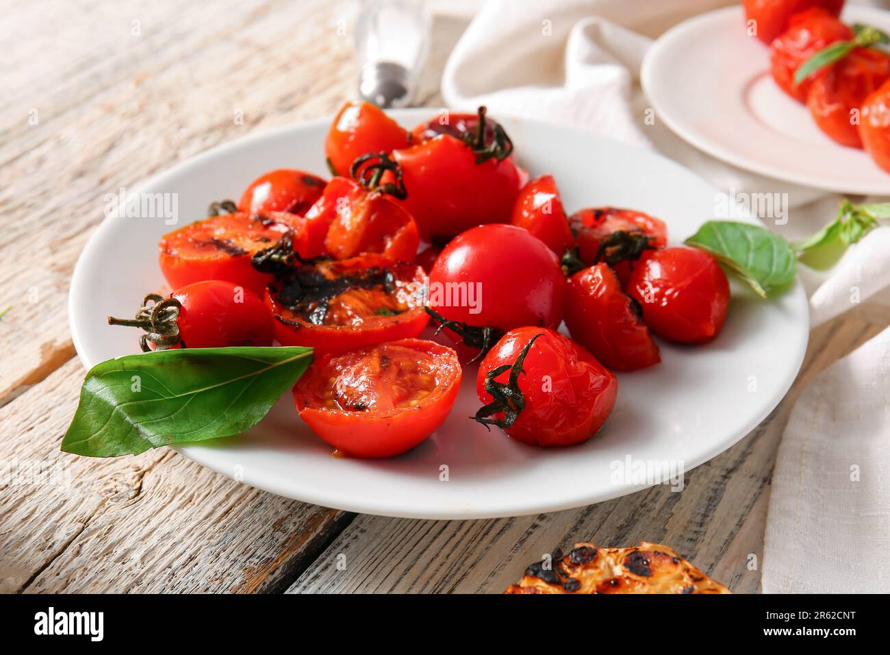 Teller mit leckeren gegrillten Tomaten und Basilikum auf weißem Holzhintergrund Stockfoto