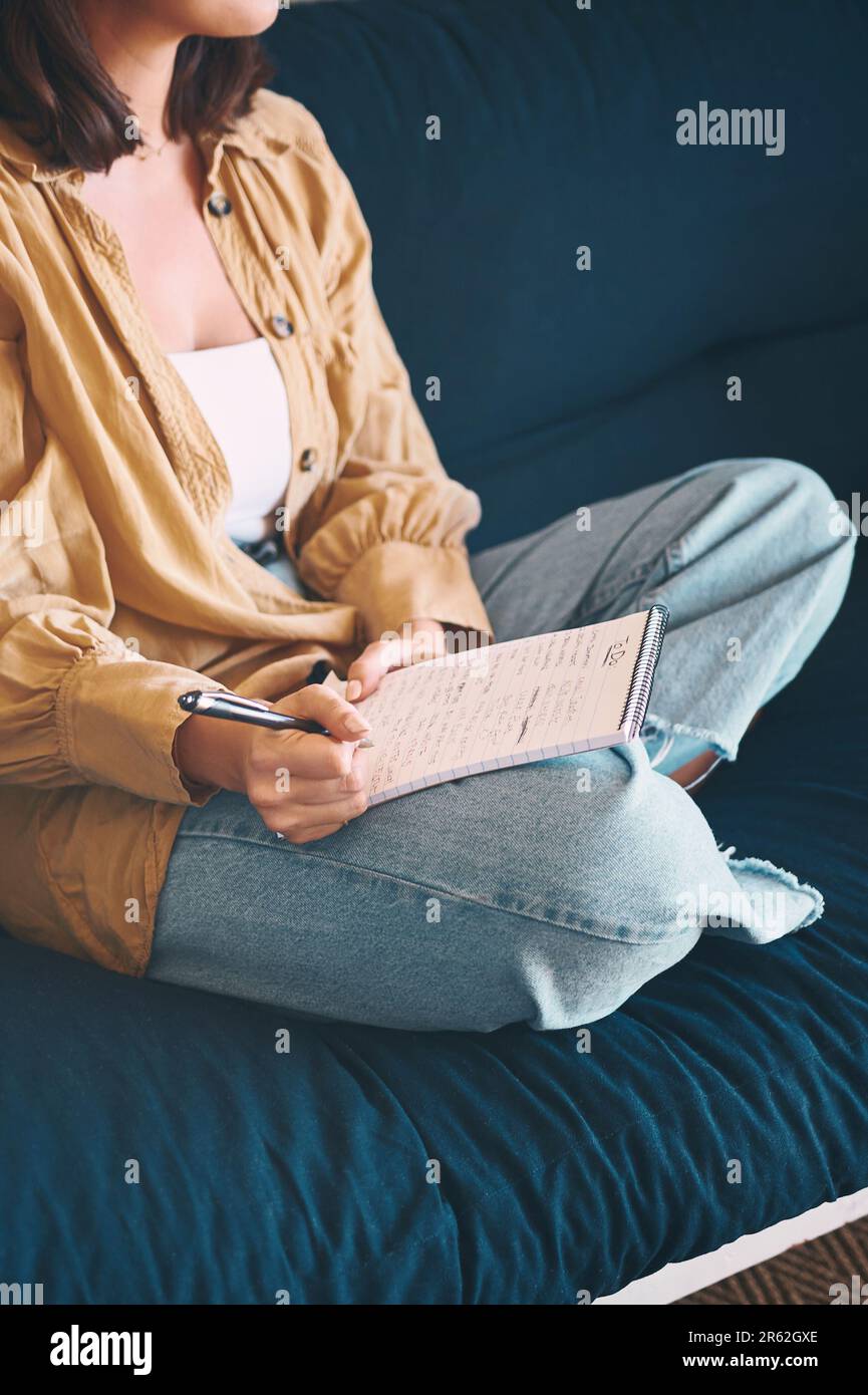 Notieren Sie sich selbst, verbringen Sie mehr Zeit mit sich selbst. Eine unbekannte Frau, die sich zu Hause auf dem Sofa entspannt und Notizen macht. Stockfoto