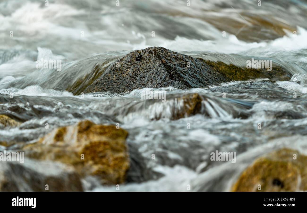 Der schnelle Quellfluss fließt über Felsen und bildet weiße Wasserwellen, Nahaufnahme - abstrakter Naturhintergrund Stockfoto