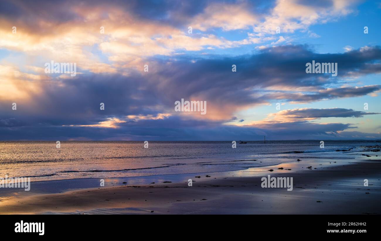 Sonnenaufgang und Sonnenaufgang über der Nordsee vor Brora Beach in Sutherland mit einem Hummerboot, das vom Hafen von Brora aus segelt Stockfoto