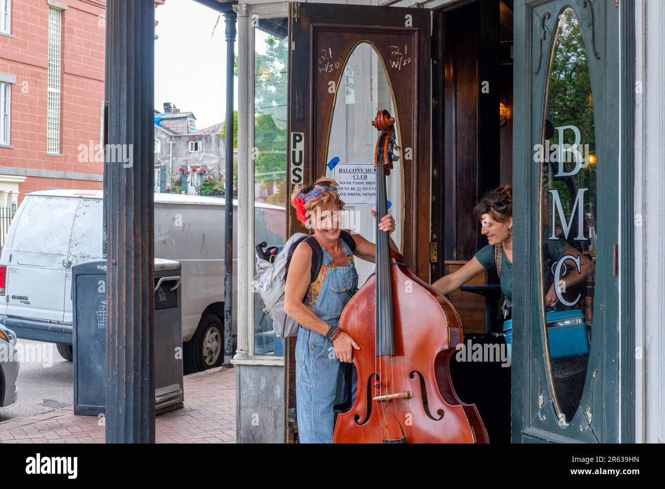 NEW ORLEANS, LA, USA - 23. APRIL 2023: Eine Bassspielerin verlässt die Vordertür des Balcony Music Clubs, während ein Freund die Tür offen hält Stockfoto