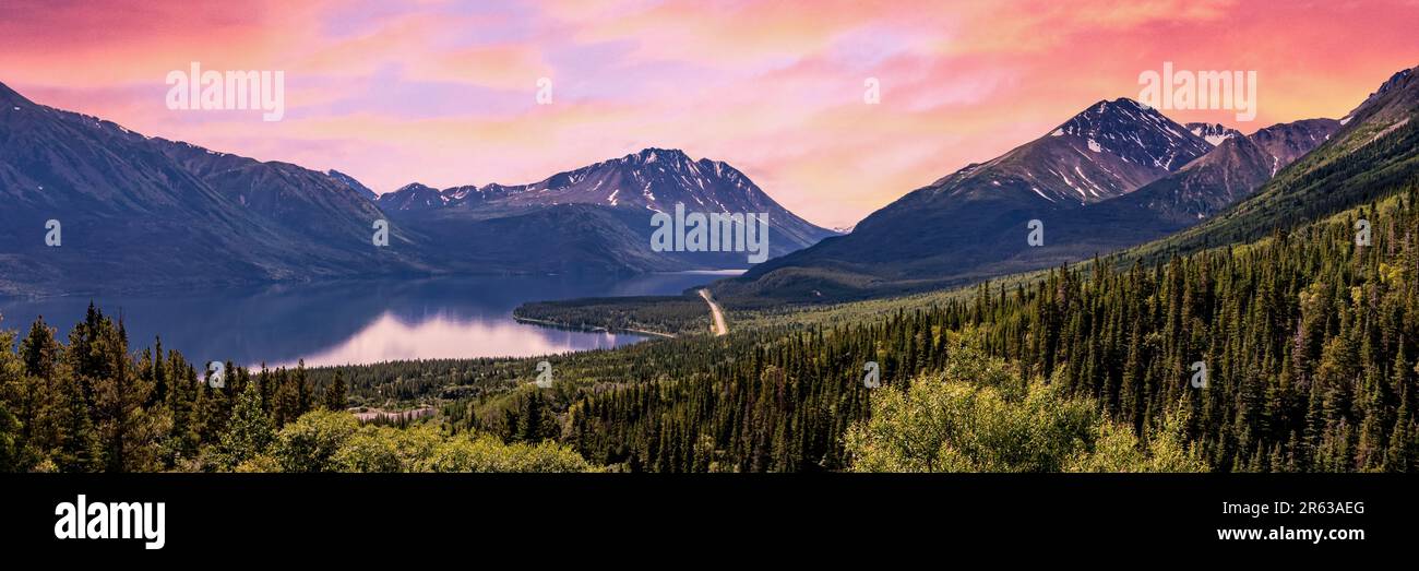 Panoramablick über eine Wildnis in der Nähe von Alaska im Sommer mit hellem rosa WolkenHimmel bei Sonnenuntergang. Malerische Landschaft in Yukon, British Columbia. Stockfoto