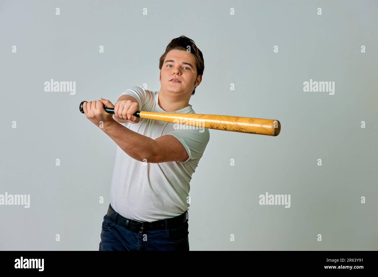 Ein Mann mit einem Schläger in der Hand schwingt auf grauem Hintergrund Stockfoto