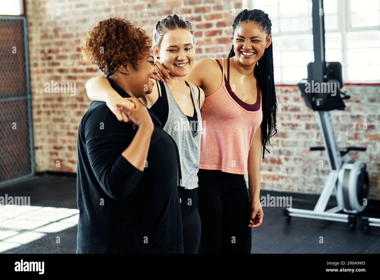 Puh, das war wirklich hart. Drei fröhliche junge Frauen unterhalten sich, während sie sich vor einem Workout im Fitnessstudio gegenseitig halten. Stockfoto