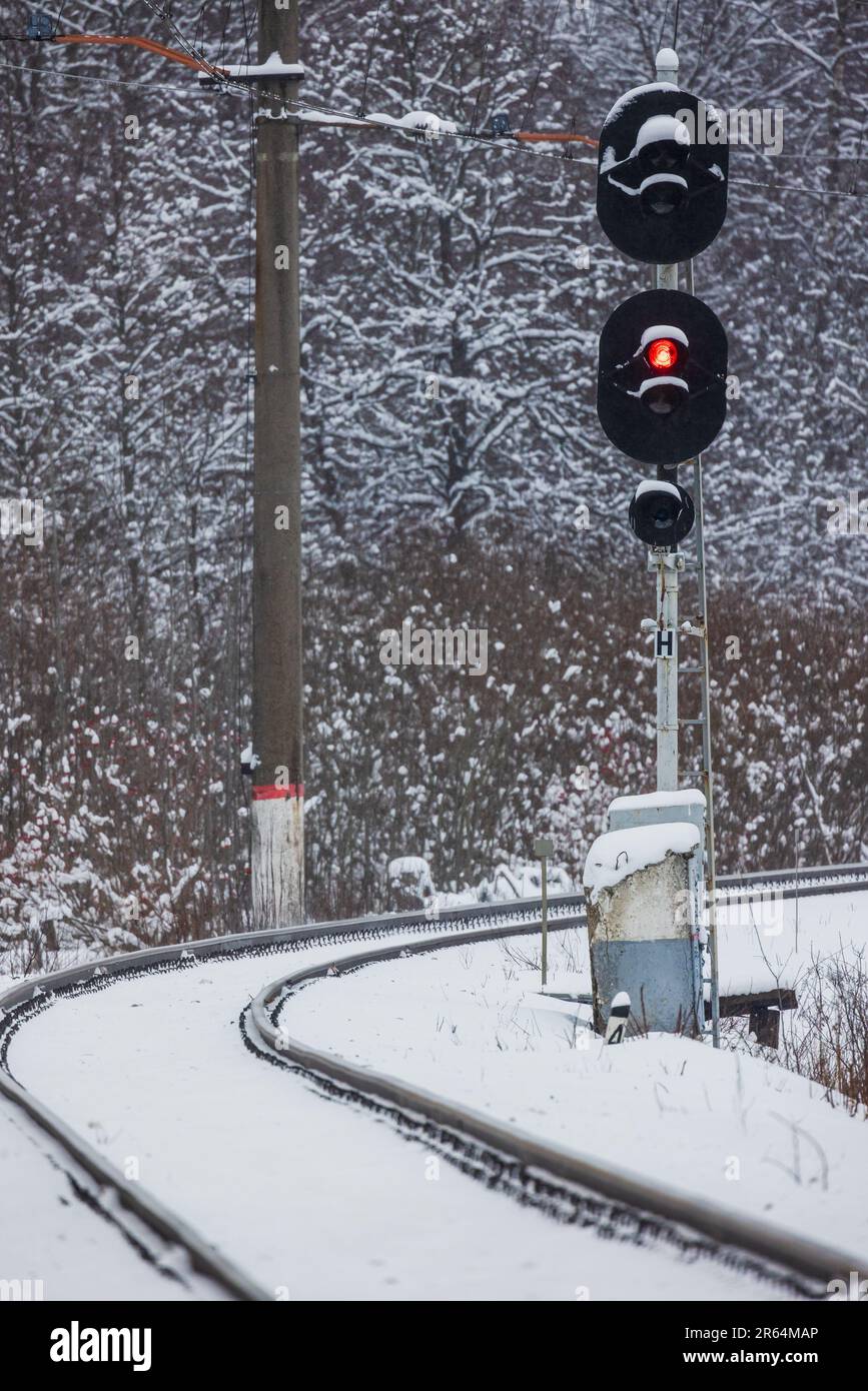 Das Eisenbahnsemaphor zeigt ein rotes Stoppsignal. Vertikales Foto an einem verschneiten Wintertag Stockfoto