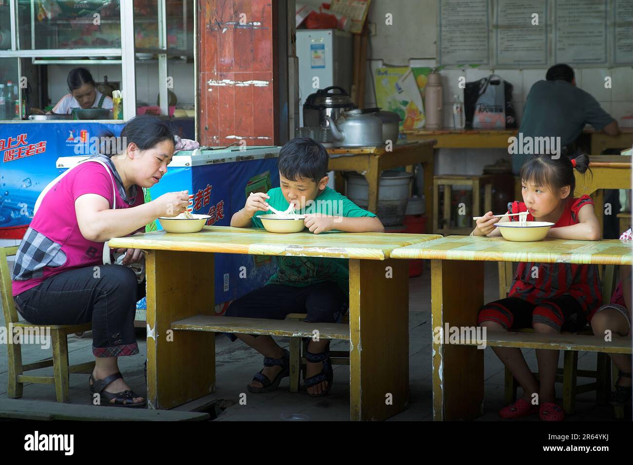 龙胜镇 (龙胜县) 中國 Longsheng, China; Eine Frau und Kinder essen in einer schmuddeligen chinesischen Bar eine Mahlzeit; Frau und Kinder essen in einer schmuddeligen chinesischen Bar Stockfoto