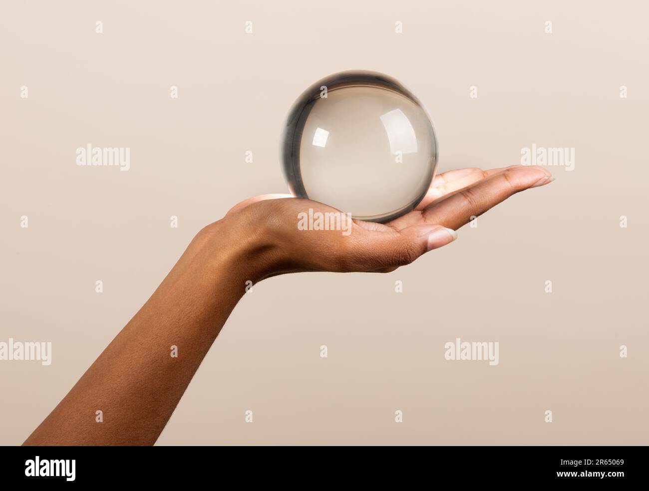 Eine nicht wiedererkennbare afroamerikanische Frau, die eine transparente Glaskugel zeigt, die einer magischen Kristallkugel ähnelt, vor einem beigen Hintergrund Stockfoto