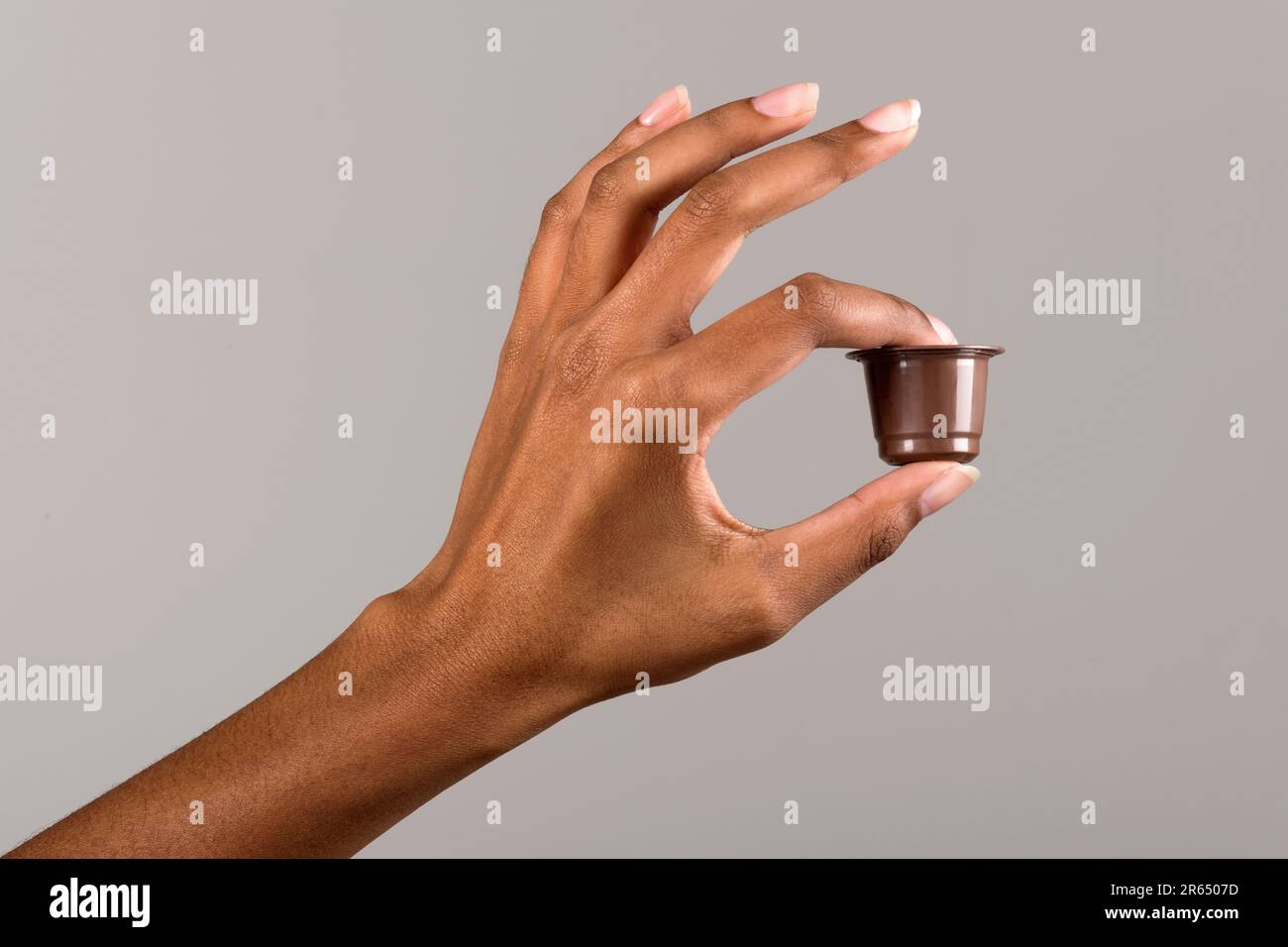 Nicht wiedererkennbare afroamerikanische Frau, die Kaffeekapsel vor grauem Hintergrund im hellen Studio vorführt Stockfoto