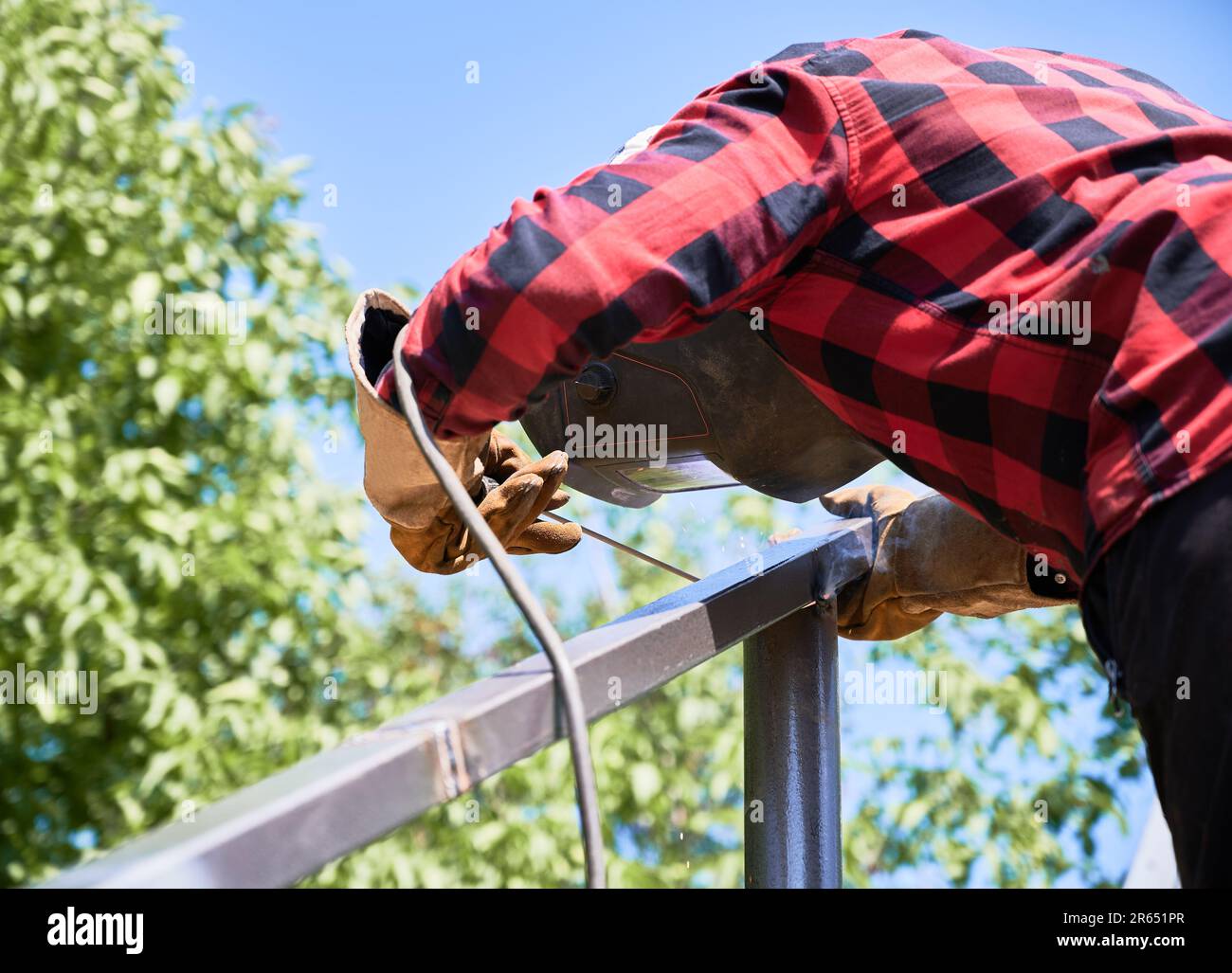 Man-Schweißstab mit Schweißmaschine zur Installation von Solarpaneelen. Schweißer am sonnigen Tag auf dem Feld im Schutzhelm. Stockfoto