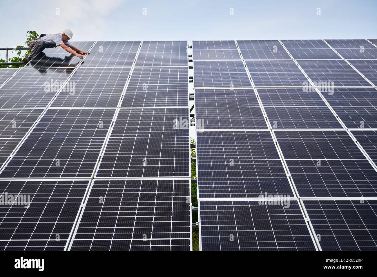 Arbeiter, der Solarpaneele installiert. Erneuerbare und ökologische Energie. Vorstellung von umweltverträglich. Moderne Technologie und Innovation. Europäischer Mann mit Arbeitskleidung und Helm. Ansicht von unten. Sonniger Tag Stockfoto