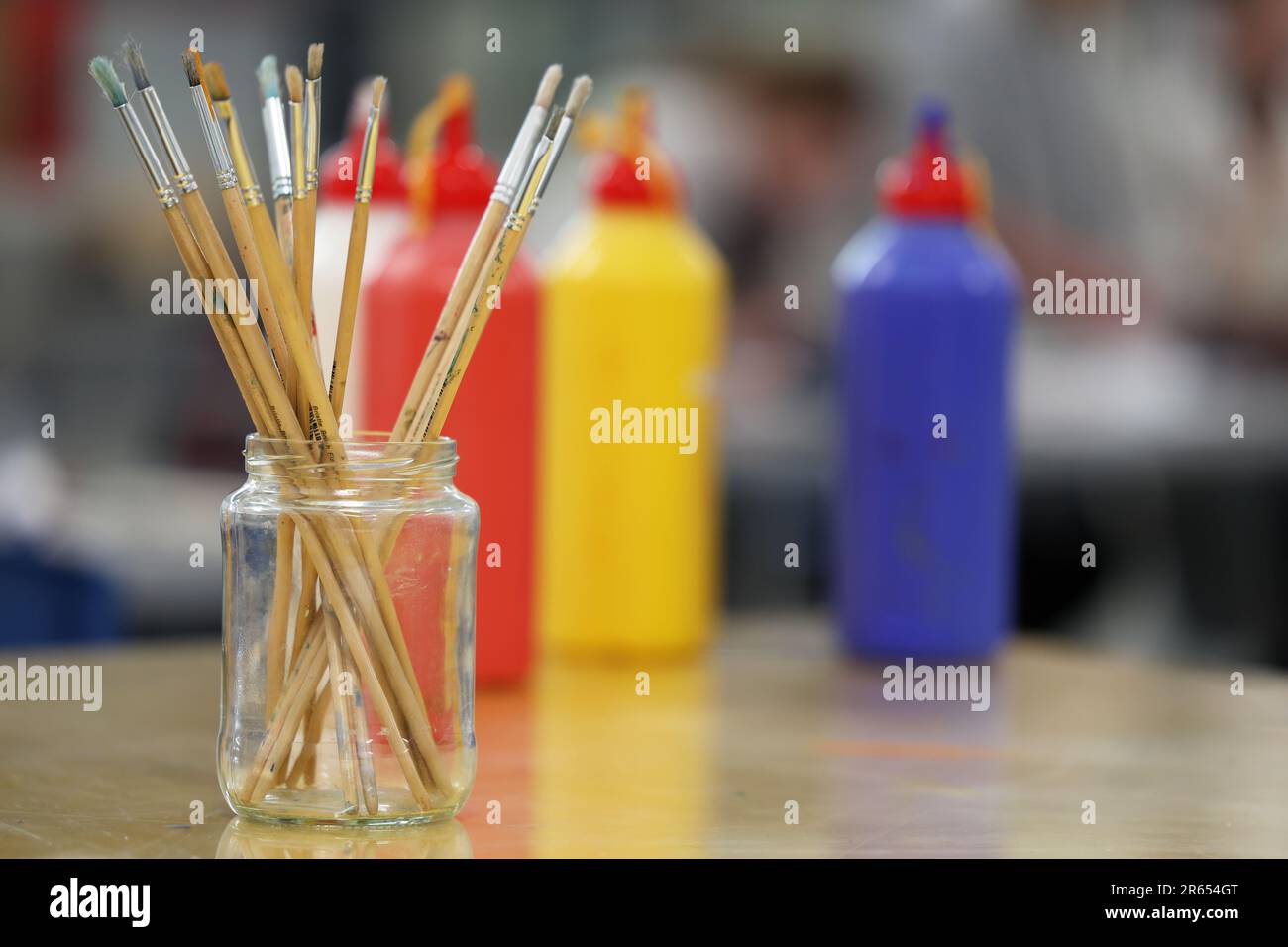 Nahaufnahme eines Klassenzimmers für visuelle Kunst mit einem Satz Pinsel, der in einem Glasgefäß steht. Primärfarben Rot, Gelb und Blau dahinter. Stockfoto