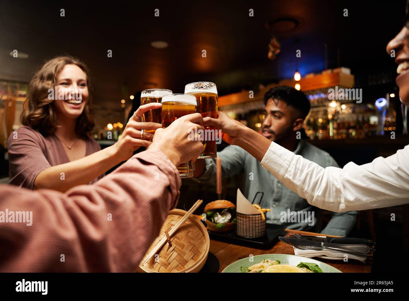 Fröhliche, junge, multiethnische Gruppe von Freunden in legerer Kleidung, die in der Bar Toast mit Bier trinken Stockfoto