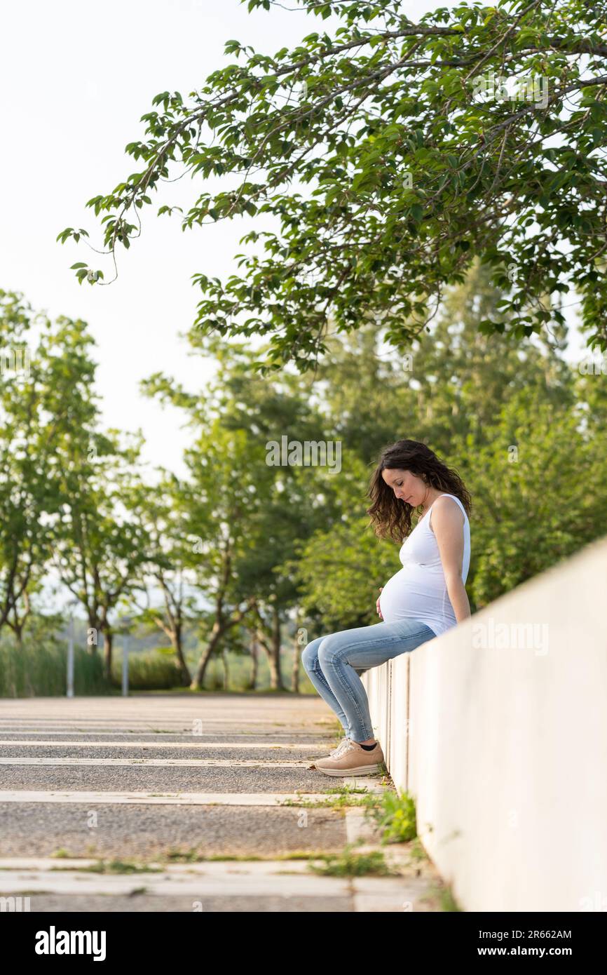 Junge schwangere Frau, die auf der Straße auf ihrem Bauch sitzt Stockfoto