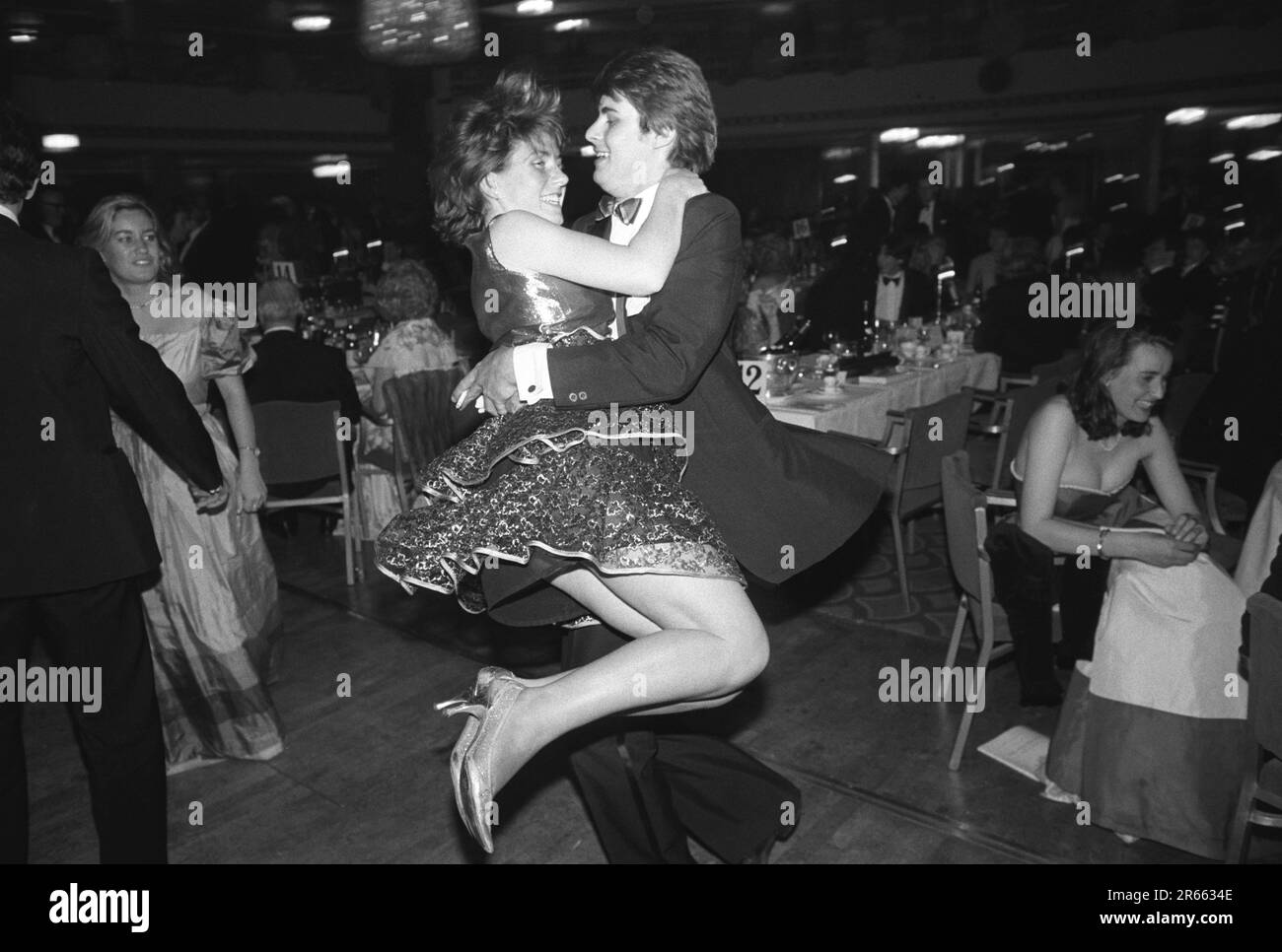Ein wohlhabendes junges Paar Sloane Rangers geht auf die Tanzfläche beim alljährlichen Rosenball der Wohltätigkeitsorganisation, der im Grosvenor House Hotel, Park Lane, stattfindet. Mayfair, London, England, ca. Mai 1982. Stockfoto