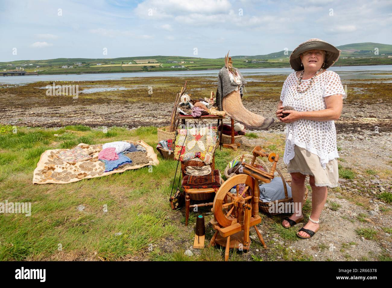 Seniorin mit Drehrad, Wollkugeln und Webartikeln im Freien in Portmagee. Valentia Island im Hintergrund. Stockfoto