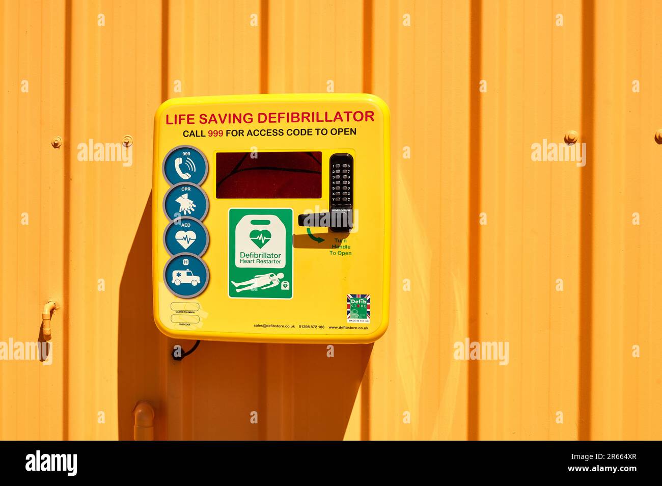 Lebensrettender gelber Defibrillator im Karton, an der orangefarbenen Wand montiert Stockfoto