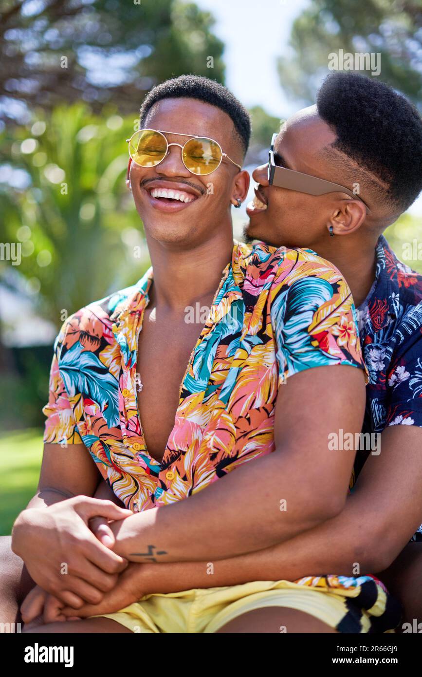 Glückliches junges schwules Paar mit Sonnenbrille, das sich umarmt und lacht Stockfoto
