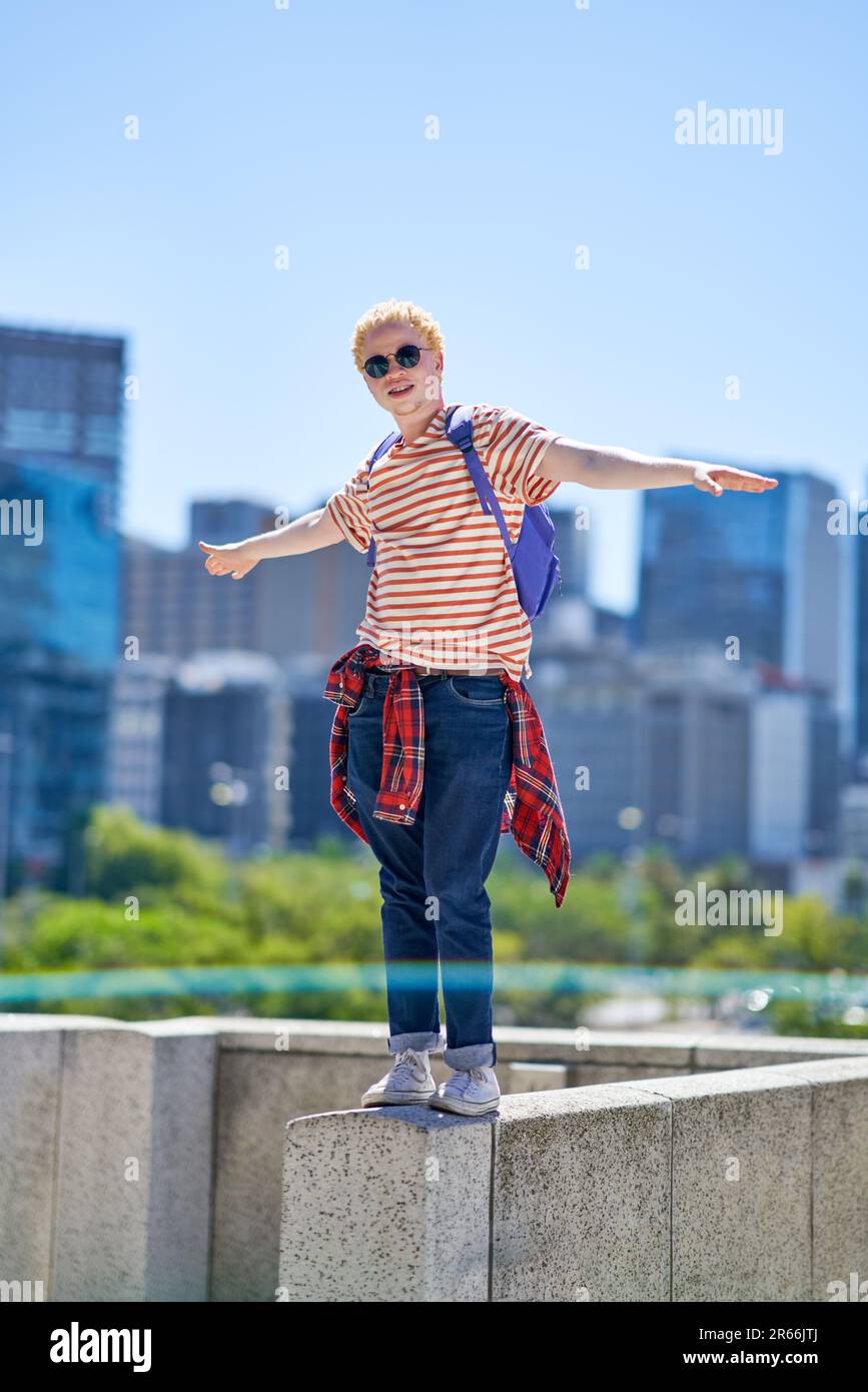 Ein cooler junger Mann, der in der sonnigen Stadt auf einem Vorsprung steht Stockfoto