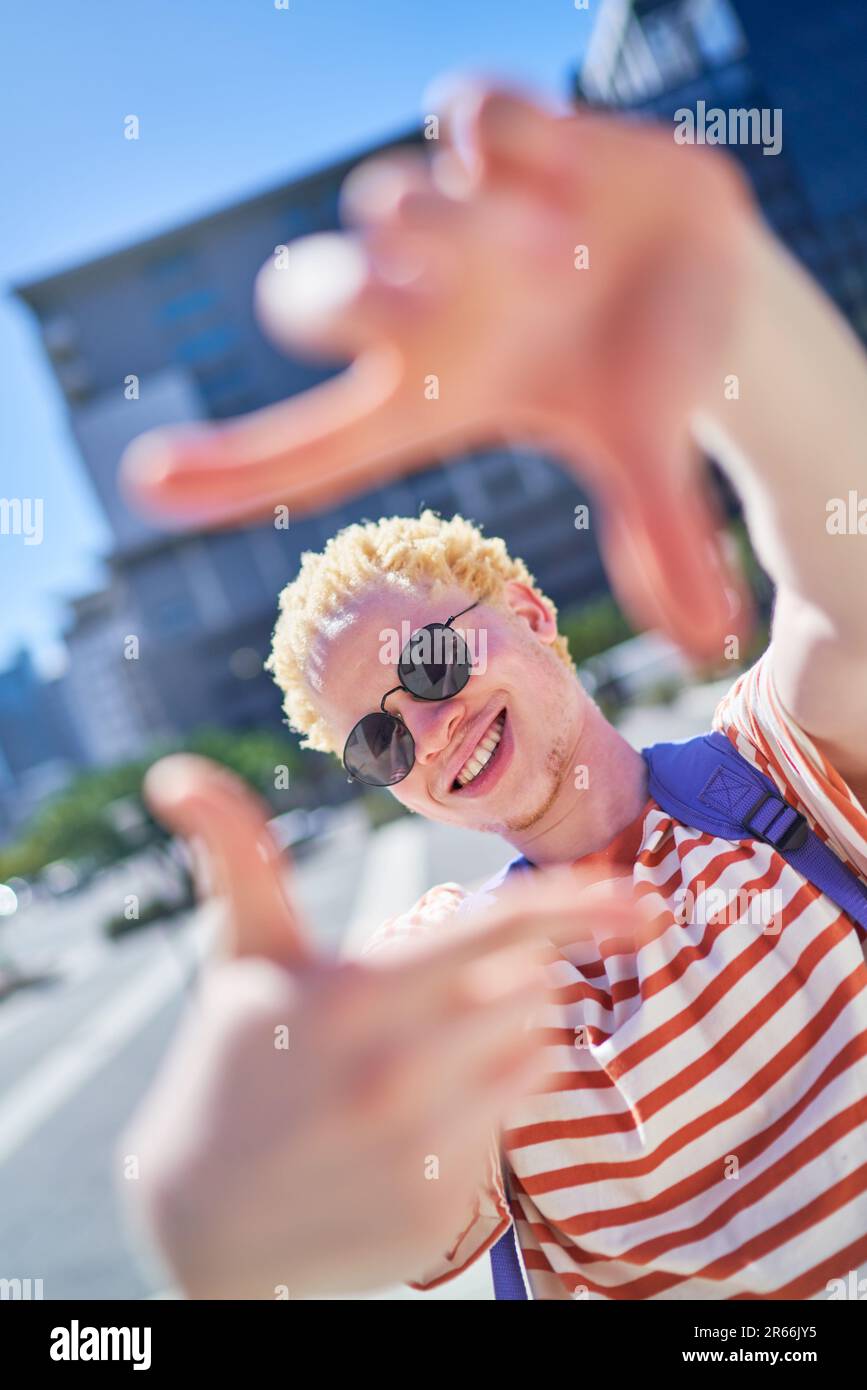 Portrait glücklicher junger Mann, der den Fingerrahmen in der sonnigen Stadt bewegt Stockfoto